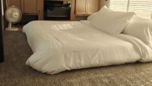 Een slaapkamer met een groot bed, houten kasten, een ventilator en een televisie.