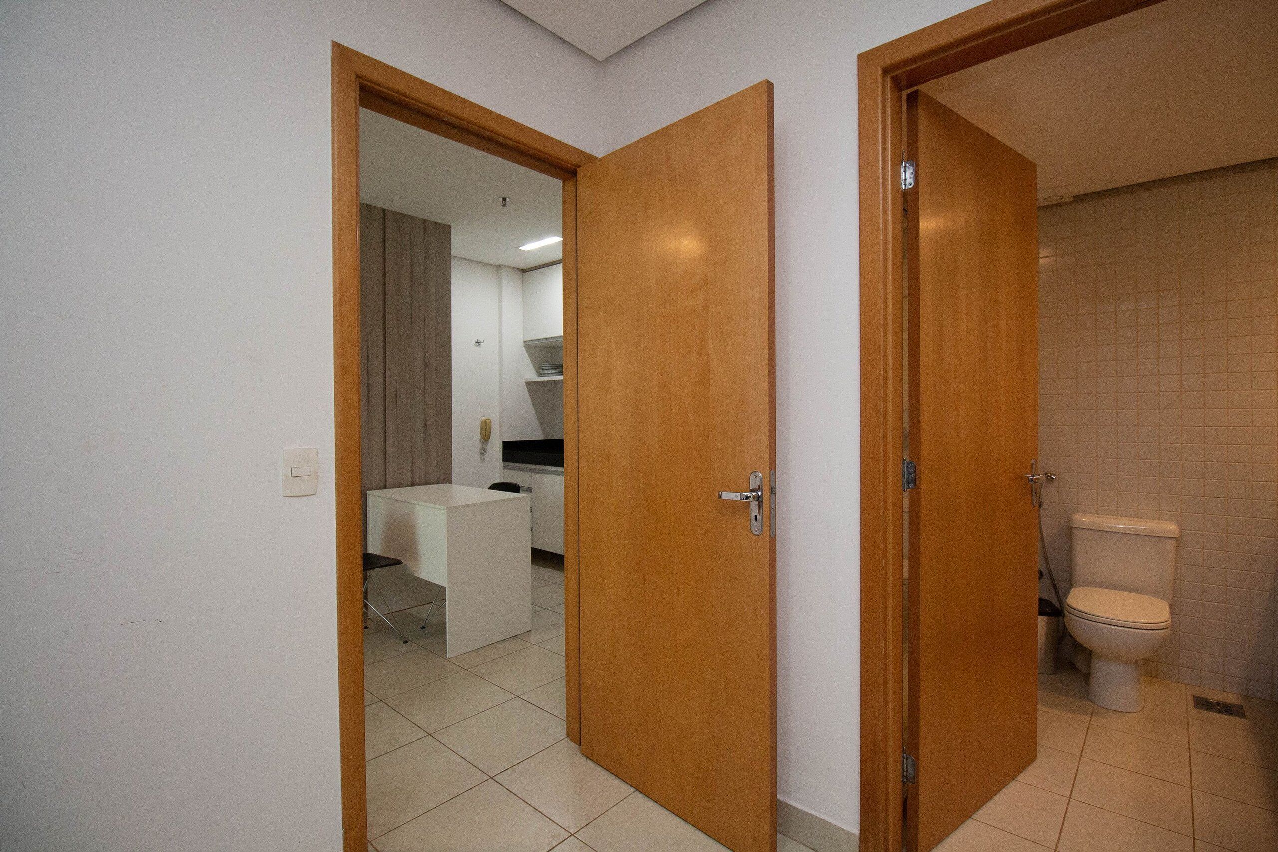 A room with a wooden door, a white desk, and a toilet.