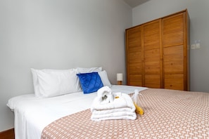 A neatly made bed with white and patterned bedding, a blue pillow, and a stack of white towels on the bed. - Close to the Underground and 10 Minutes From the Beach Mfb302 (Rio de Janeiro)