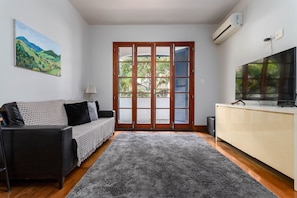 A living room with a sofa, a TV, a large window, and a painting on the wall. - Close to the Underground and 10 Minutes From the Beach Mfb302 (Rio de Janeiro)
