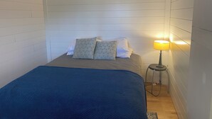 Un llit amb llençol blau, almoines i una làmpada de nit en una habitació amb parets blanques de quadres.