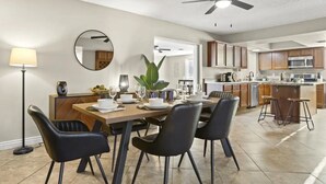 A modern kitchen with wooden cabinets, a microwave, and a dining area with a table set for four. - Large Pool, Near State Farm STDM and Many Entertainment Districts! (Peoria)