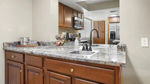 A kitchen with granite countertops, wooden cabinets, a stainless steel sink, and a microwave. - Large Pool, Near State Farm STDM and Many Entertainment Districts! (Peoria)