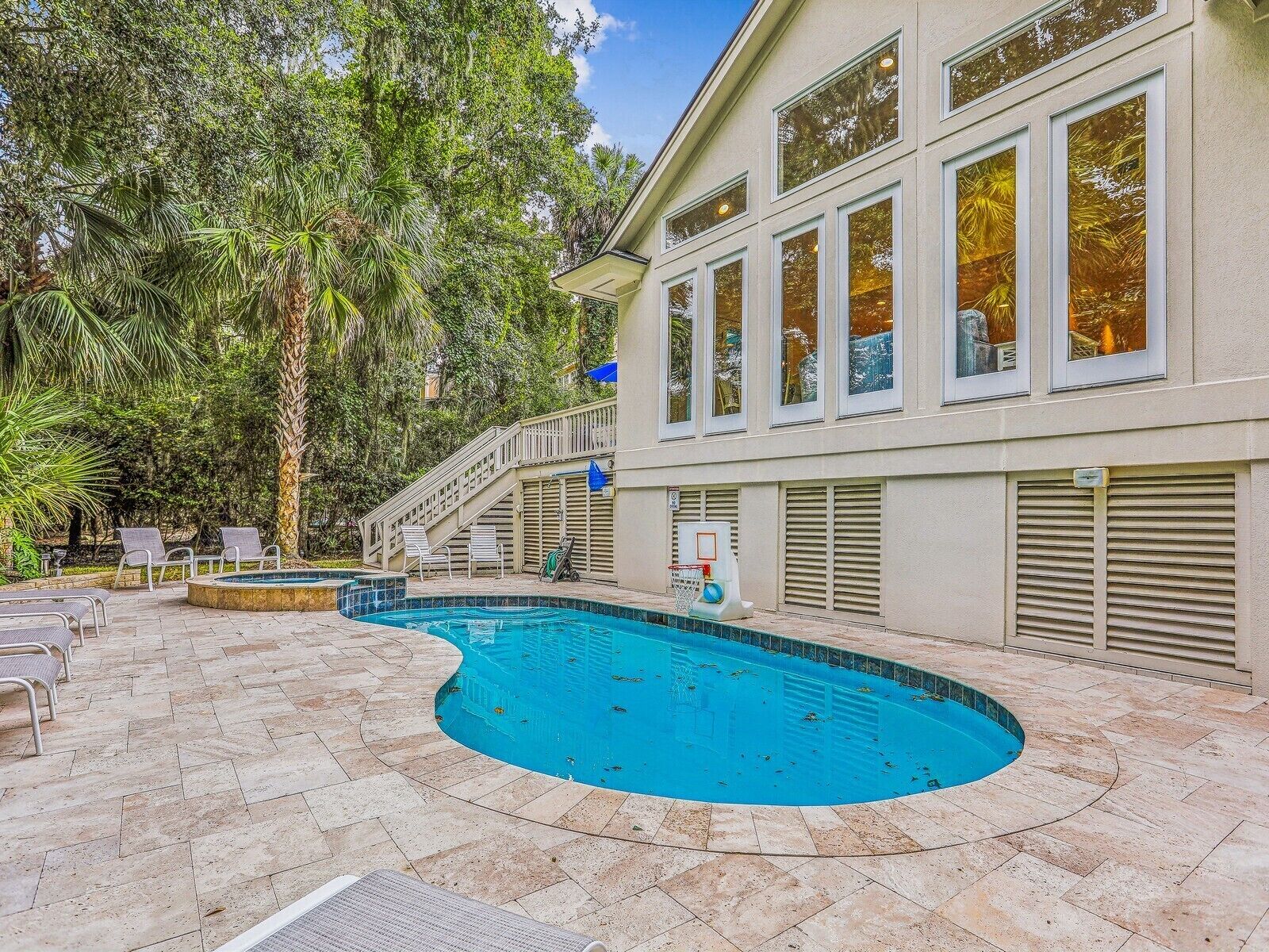 A swimming pool with a curved edge, surrounded by lounge chairs and a staircase leading to a building with large windows.