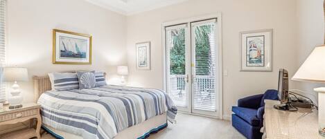 A bedroom with a large bed, two bedside tables with lamps, a blue sofa, and a wicker side table.
