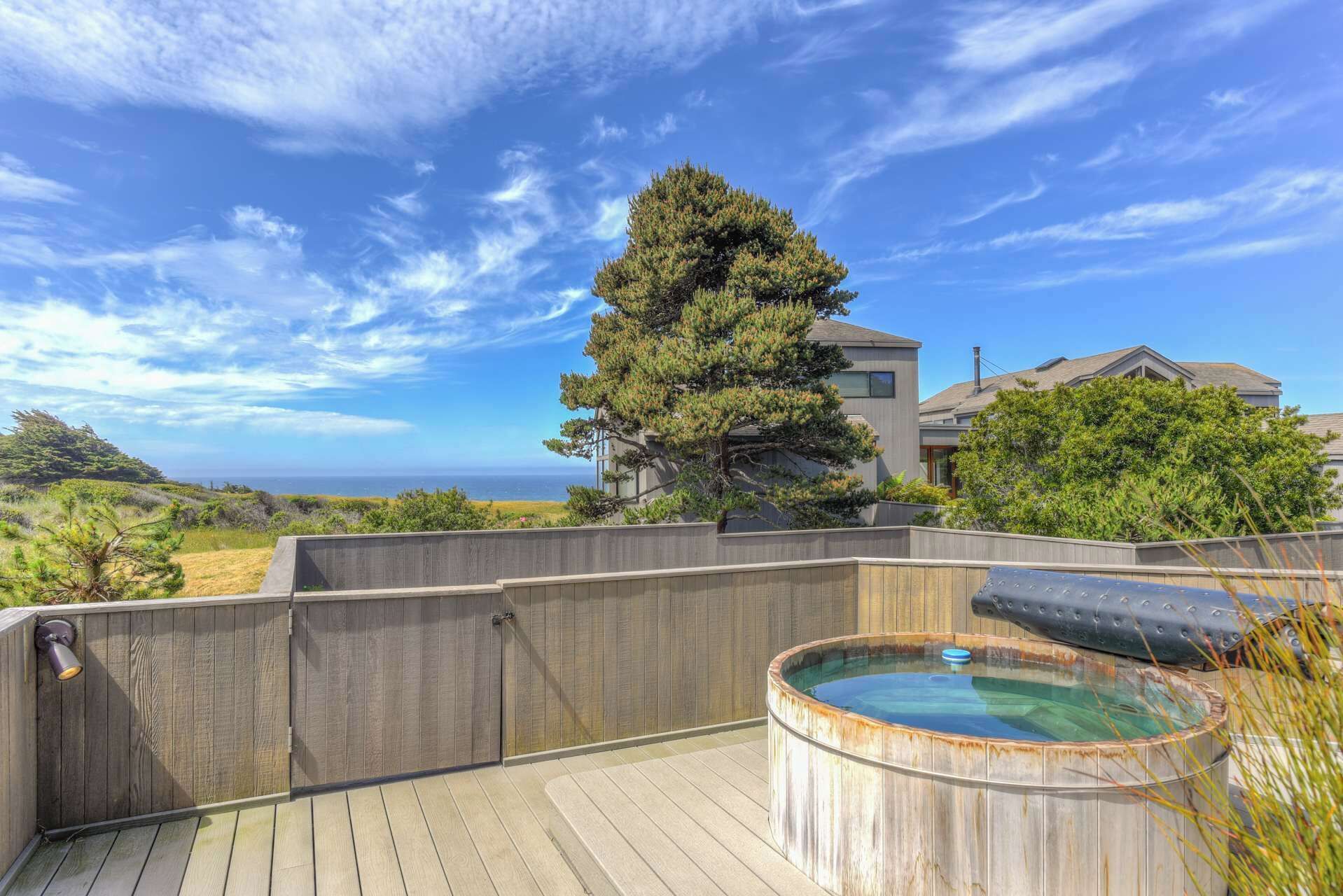 A wooden deck with a hot tub, a large tree, and a view of the ocean.
