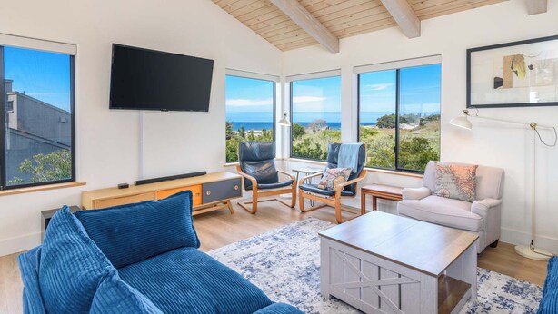 Sala de estar ampla com uma televisão grande, assentos confortáveis e vista para o mar.
