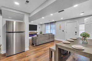 A modern kitchen with a stainless steel refrigerator, a grey sofa, and a wooden dining table with plates. - Game Room | High Speed WIFI | EV Charger | Keurig (Seaside Heights)