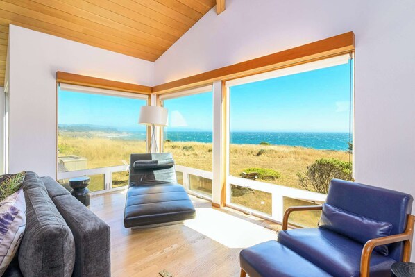 A room with a view of the ocean, a sofa, a chair, and a lamp.