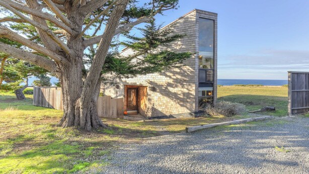 A modern house with a stone facade, a wooden door, and a view of the ocean. - Sea Pine | Hot Tub with Ocean View (Sea Ranch)