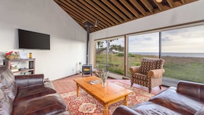 A modern living room with leather sofas, a wooden coffee table, and a large window offering a view of the outdoors. - Sea Pine | Hot Tub with Ocean View (Sea Ranch)