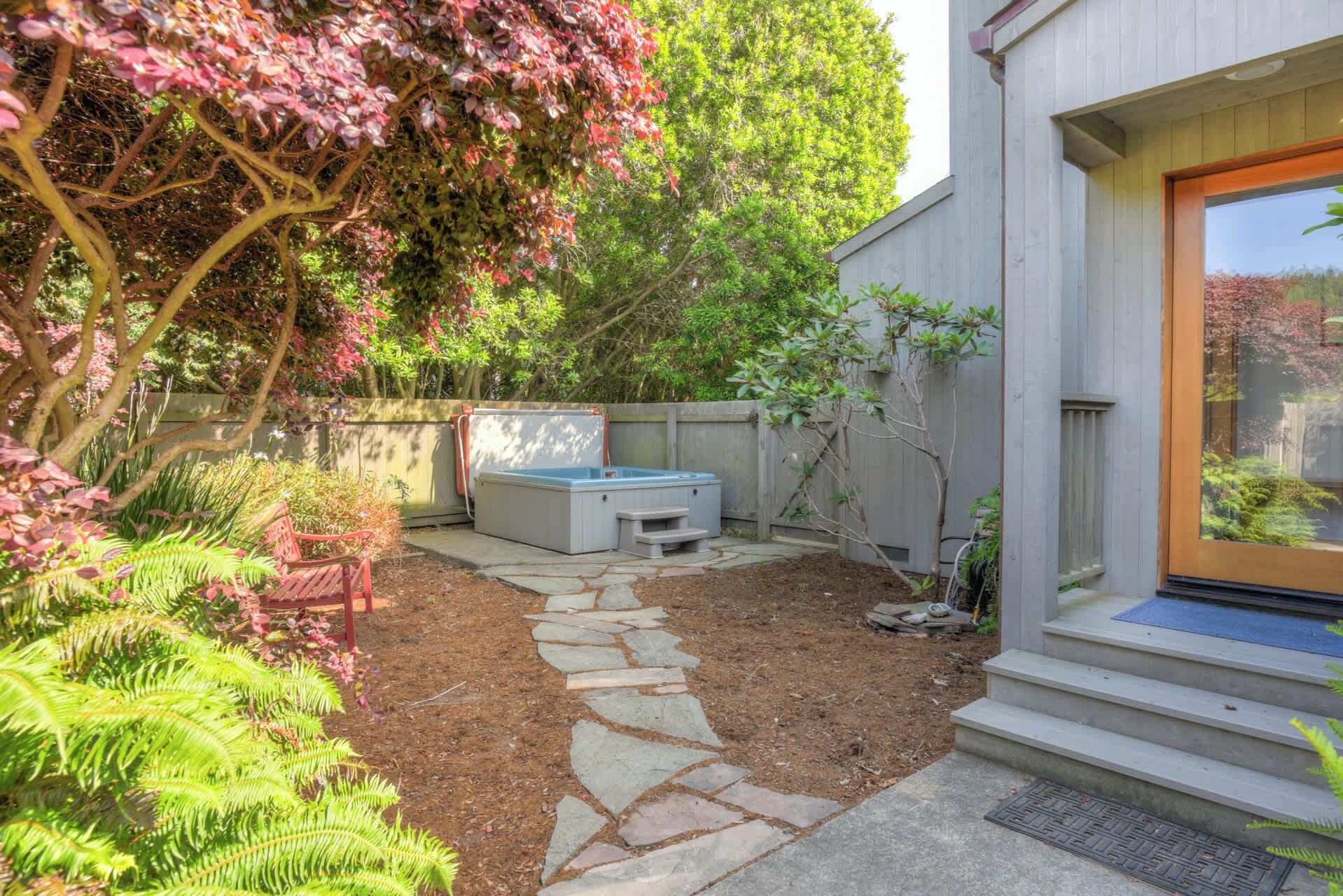 A backyard with a hot tub, stone pathway, and a wooden deck.