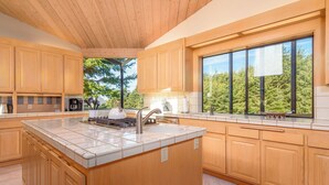 Una cocina moderna con armarios de madera, una isla grande con estufa y un ventanal con vistas a árboles.