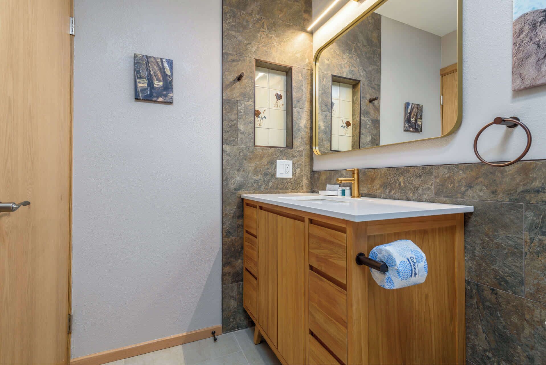 A bathroom with a wooden vanity, a white sink, a mirror, and a towel dispenser.