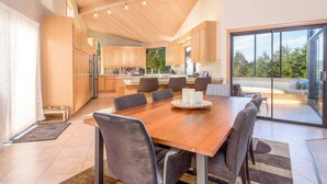 Una cocina moderna con armarios de madera y una isla grande, un comedor con mesa y sillas de madera, y un ventanal corredero que da a un balcón con vistas a árboles.