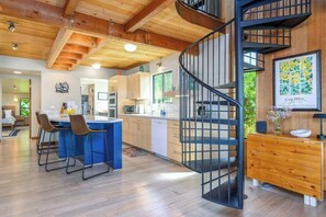 Une cuisine moderne dotée d’un îlot central, de poutres en bois au plafond et d’un escalier en colimaçon.