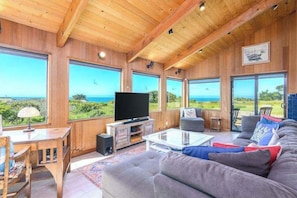 Un intérieur en bois avec une télévision, un canapé et de grandes fenêtres donnant sur un paysage magnifique.