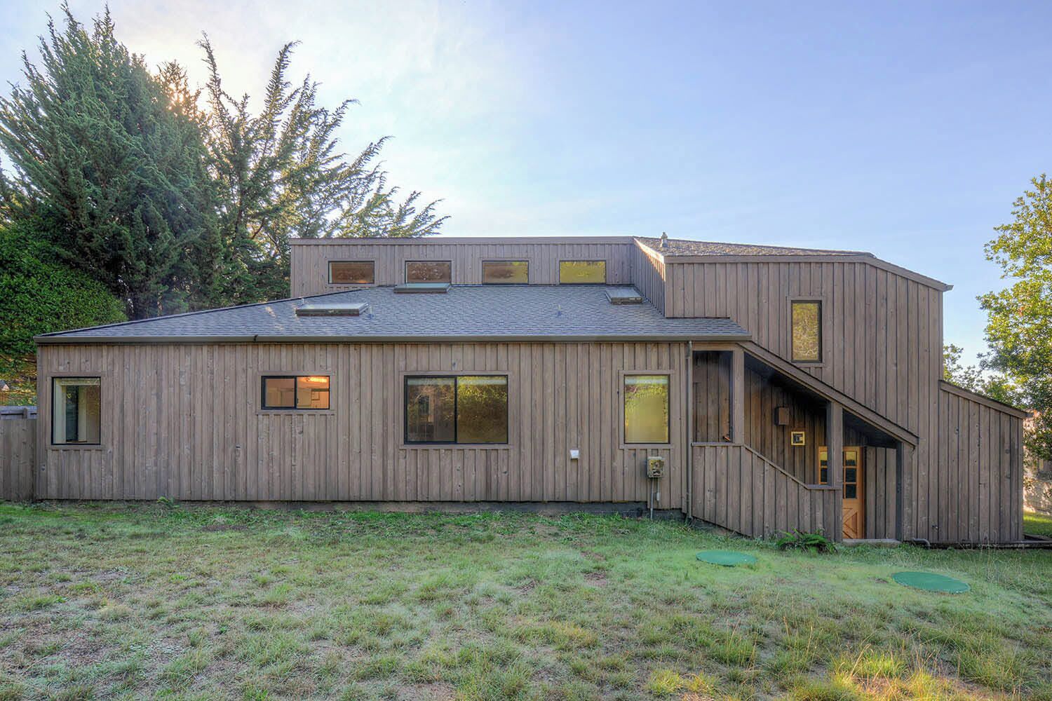 A modern wooden house with a flat roof, large windows, and a small porch.