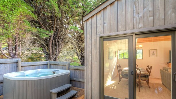 A hot tub on a wooden deck with a glass door leading to an indoor dining area.