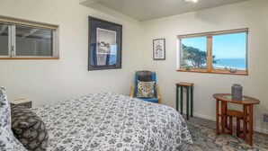 Une chambre à coucher comprenant un lit, une chaise, une petite table, une fenêtre donnant sur un paysage agréable et un luminaire au plafond.
