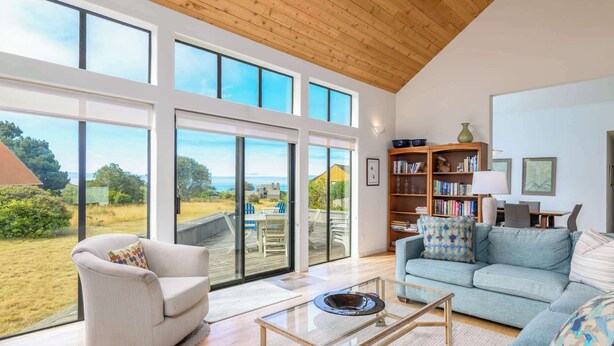 A spacious living room with a large glass door leading to a deck, a comfortable sofa, a coffee table, and a bookshelf. - Soak in Ocean Views at Blair w/ Hot Tub! (Sea Ranch)