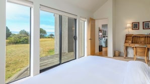 A bedroom with a large bed, a wooden dresser, and a view of a grassy field through sliding glass doors. - Soak in Ocean Views at Blair w/ Hot Tub! (Sea Ranch)