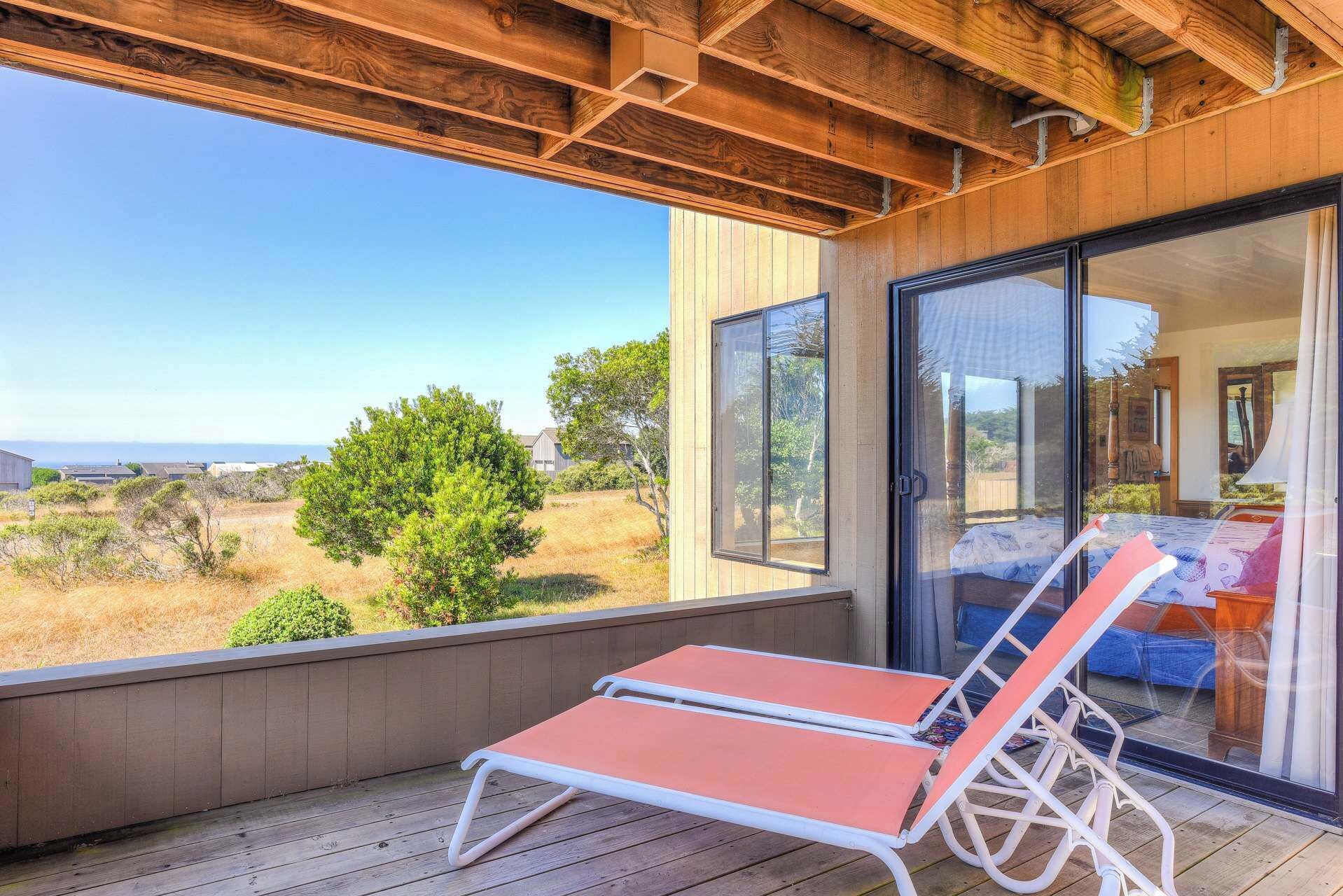 Ein Balkon mit Holzboden, eine Glastür zu einem Schlafzimmer und Blick auf die Landschaft.