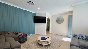 A modern living room with a sofa, a coffee table, and a flat-screen TV mounted on the wall. - Broadwater Beach Cottage (Broadwater)