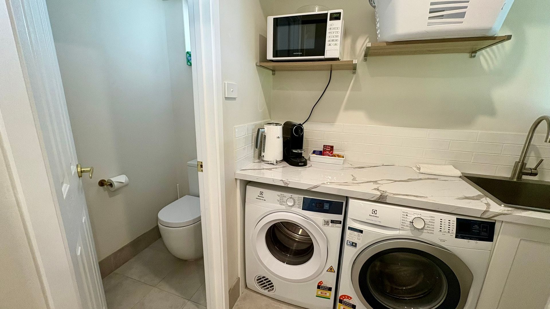 A compact laundry room with a washing machine, a microwave, and a small shelf.