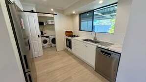A compact kitchen with a dishwasher, stove, microwave, and washing machine. - Broadwater Beach Cottage (Broadwater)