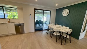 A modern kitchen with a dishwasher, a dining area with a table set for six, and a large wall clock. - Broadwater Beach Cottage (Broadwater)