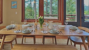Mesa de comedor dispuesta para seis personas con vistas a árboles a través de amplios ventanales.