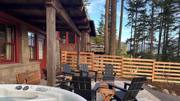 Un jacuzzi con sillas y una mesa, rodeado por una terraza de madera y un muro de piedra.