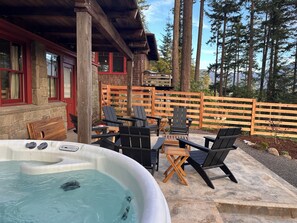 A hot tub with chairs and a table, surrounded by a wooden deck and a stone wall. - Huckleberry House - New Listing! (Eastsound)