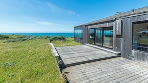 A modern building with large windows overlooking a grassy area and the ocean.
