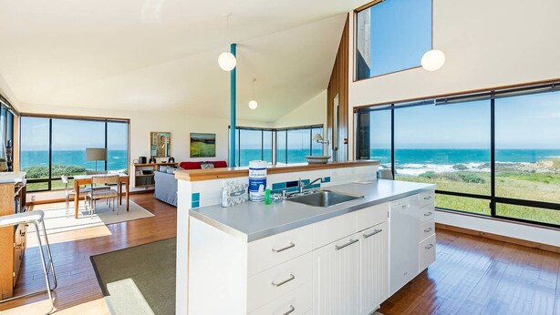 A modern kitchen with large windows, a dining area, and a view of the ocean.