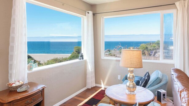 A balcony with a view of the ocean, a round table with a lamp, a sofa, and a small wooden table with a decorative item. - Lucky Ewe - Gualala | 3BR | Ocean Views | Sleeps 6 (Gualala)