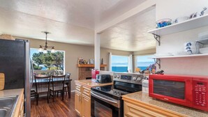 A kitchen with wooden cabinets, a red microwave, a stove, and a dining area with chairs and a table. - Lucky Ewe - Gualala | 3BR | Ocean Views | Sleeps 6 (Gualala)