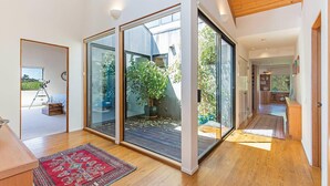 A modern interior with large sliding glass doors leading to a balcony, a wooden floor, and a red patterned rug. - Grateful Getaway | Fireplace and Scenic Views (Sea Ranch)