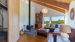 A modern living room with a fireplace, wooden flooring, a sofa set, and a bookshelf. - Grateful Getaway | Fireplace and Scenic Views (Sea Ranch)