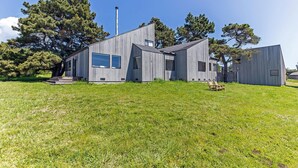 A modern, single-story house with a sloped roof, large windows, and a chimney. - Grateful Getaway | Fireplace and Scenic Views (Sea Ranch)