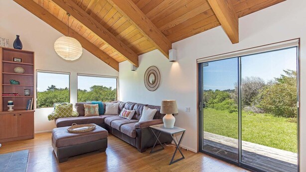 A modern living room with a wooden ceiling, a sectional sofa, a side table, and a large sliding glass door leading to a grassy outdoor area. - Grateful Getaway | Fireplace and Scenic Views (Sea Ranch)