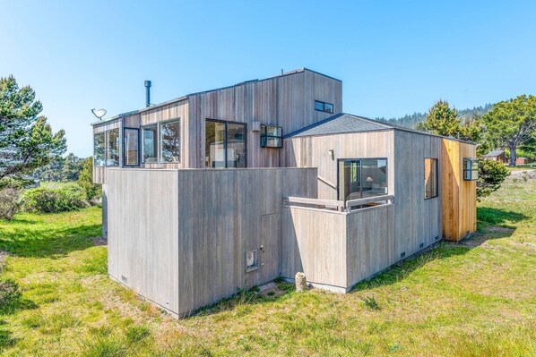 Eine moderne Holz-Blockhütte mit großen Fenstern, einem Flachdach und einer kleinen Terrasse.