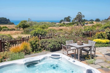 Bask in the serene backyard retreat with a hot tub and distant ocean views under a clear blue sky