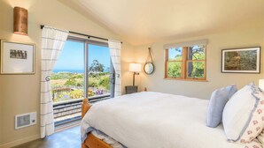 A bedroom with a large bed, a view of the outdoors, a lamp, and framed pictures on the walls. - Sea Ranch 3BR | Trails, Hot Tub, EV | For 6 (Sea Ranch)