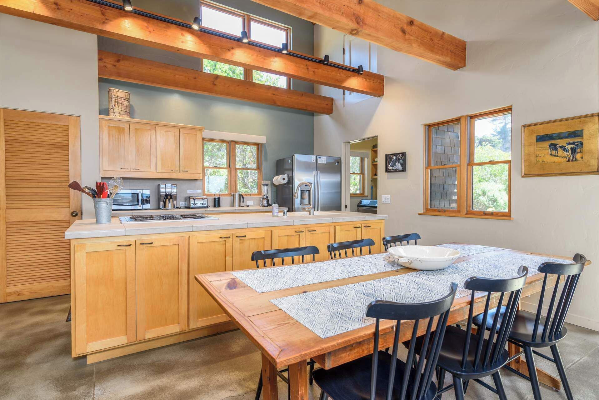 A modern kitchen with wooden cabinets, a stainless steel refrigerator, and a dining area with a wooden table and chairs.