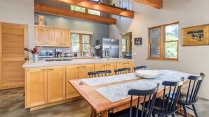 A modern kitchen with wooden cabinets, a stainless steel refrigerator, and a dining area with a wooden table and chairs. - Sea Ranch 3BR | Trails, Hot Tub, EV | For 6 (Sea Ranch)