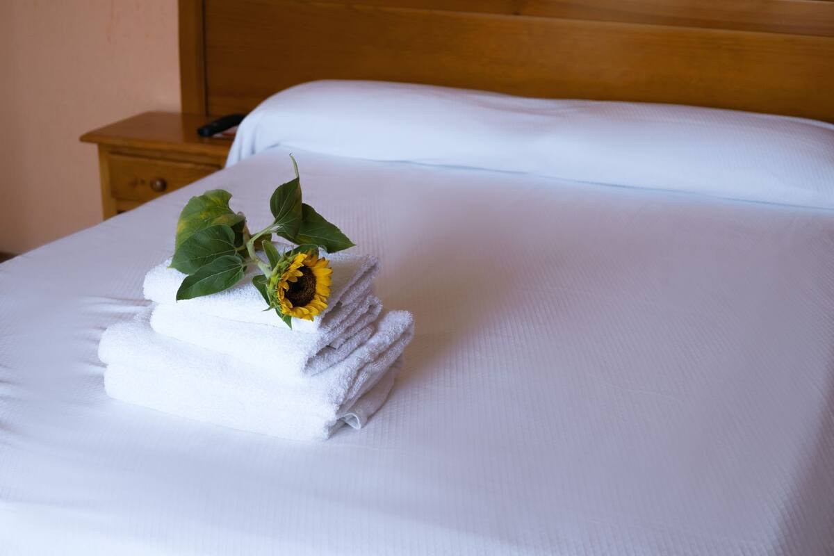 A neatly made bed with white linens and a sunflower on top.