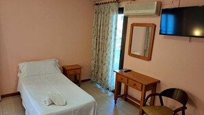 Una habitación de hotel con una cama, un escritorio, una silla, un televisor y un aire acondicionado.
