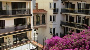 Un edificio residencial de varios pisos con balcones, un pequeño patio interior y un arbusto floreciente de color rosa al frente.